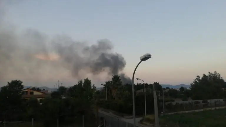 Fiamme in un terreno, fumo nero invade città. Foto e video
